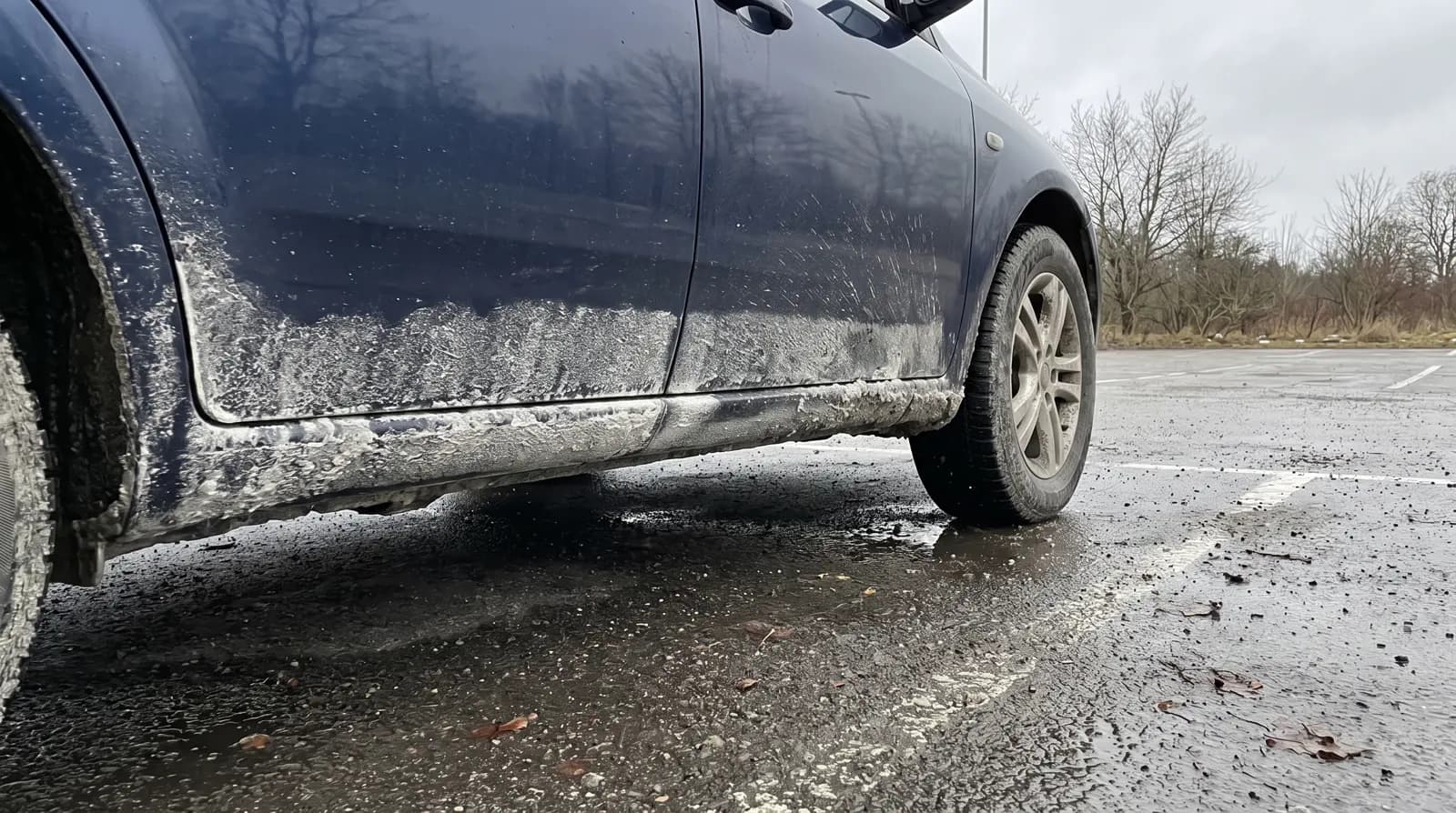 Intorkat vägsalt och slask på tröskel och hjulhus på en mörkblå bil en vinterdag